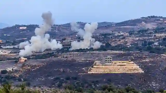 Large smoke plumes rising from targeted compound across rural valley landscape