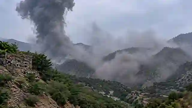 Massive dark smoke plume rising from rugged mountain terrain following a tactical airstrike impact