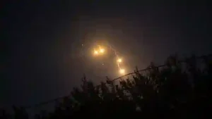 Middle East security summit delays: Glowing illumination flares and smoke trails falling through dark night sky above tree line