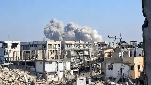 Heavy rubble and destroyed multi-story concrete buildings with massive smoke rising in the background